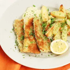 Krispiga bitar av pankopanerad zucchini serveras med ugnsrostade potatisklyftor, en klick sås och en citronskiva.