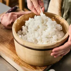 En person blandar nykokt ris i en träskål. En påminnelse om var kommer ris ifrån och hur det förbereds för sushi.