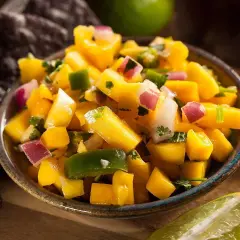 En skål med färgglad mango sallad, med tärnad mango, rödlök, grön paprika och koriander. Serveras med tortillachips och lime.