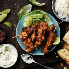 Tandoori kyckling på spett, serverad med ris, naanbröd, raita och limeklyftor.