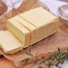 Smörblock skuret i bitar på bakplåtspapper, med rosmarin och vitlök i bakgrunden. Tänk dig att detta smör förvandlas till klarifierat smör, eller ghee, för en rikare smak.