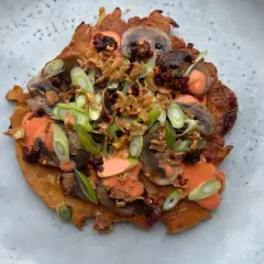 En krispig japansk kålpannkaka toppad med champinjoner, salladslök, krispiga lökar och en krämig sås.