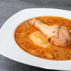 En vit skål med en kycklingklubba och potatis i en krämig, kryddig sås. En härlig chicken massaman.