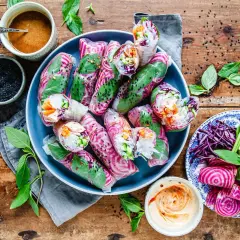 Färgglada vietnamesiska vårrullar med grönsaker och risnudlar, serverade med dippsåser och färska örter på en träbakgrund.
