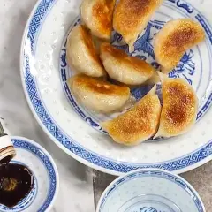 Stekta vegetariska dumplings serveras på en blåvit tallrik. Sojasås hälls upp i en liten skål. Ett perfekt vegetariska dumplings recept!