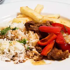 En tallrik med lomo saltado: ris, pommes frites, strimlat nötkött, rödlök och röd paprika.