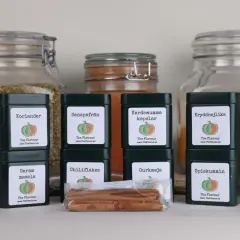 En samling mörkgröna burkar med kryddor, inklusive Garam Masala, som förbereder för en indisk kryddblandning.