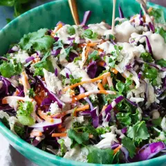 En fräsch kycklingsallad med rödkål, morötter och grönkål, toppad med en krämig dressing. En flaska kycklingfond syns i bakgrunden.