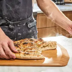 En person i förkläde håller upp en bit av en nybakad, ångande ramazan pidesi. Brödet är gyllene med sesamfrön.