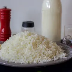 En hög med fluffigt, nykokt långkornigt ris på en tallrik. Bredvid står en röd pepparkvarn och en flaska mjölk.