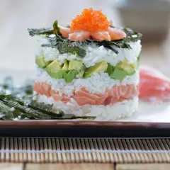 En vacker sushi tårta med lax, avokado och ris, toppad med rom och nori. En festlig rätt för alla sushiälskare.