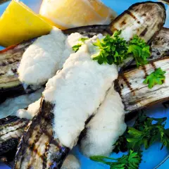 Grillad aubergine med en krämig sås och färsk persilja, serverad med citronklyftor. En härlig sommarrätt.