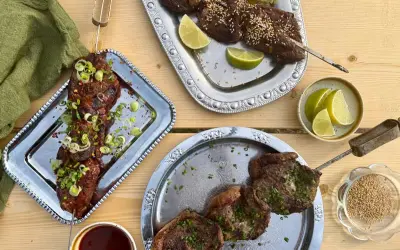 Grillad koreansk råbiff på spett, toppad med salladslök och chiliflakes. Serveras med limeklyftor och en skål sesamfrön.
