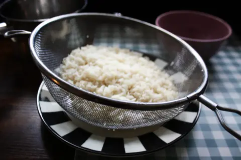 Ris i durkslag, redo att sköljas. För att koka ris med mycket vatten är det viktigt att skölja det först.