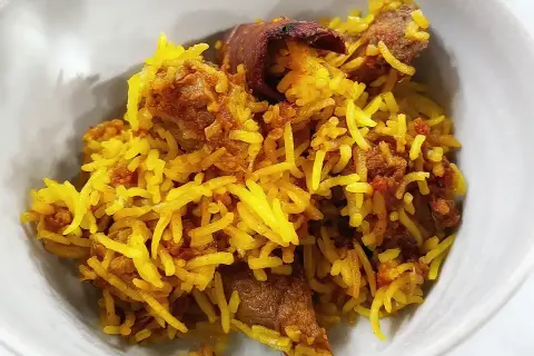 En skål med gyllene ris och möra bitar av lammkött. En härlig lamm biryani som ser otroligt god ut.
