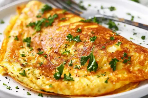 En gyllene omelett, perfekt för ett snabbt omelett recept. Garnerad med färsk persilja och serverad på en vit tallrik med en gaffel.