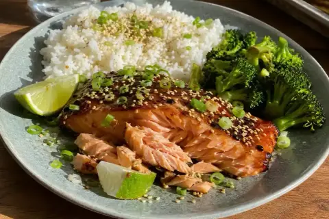 En läcker tallrik med asiatisk lax i ugn, serverad med ris, broccoli och limeklyftor.