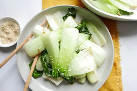 Enkel pak choi recept med sesamfrön. Grönsakerna är serverade på en tallrik med ätpinnar.