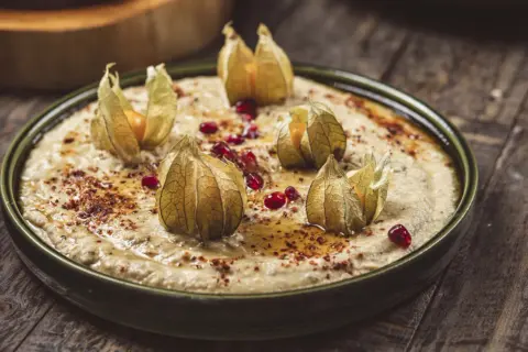 Krämig baba ganoush toppad med physalis och granatäppelkärnor, serverad på en rustik träyta.