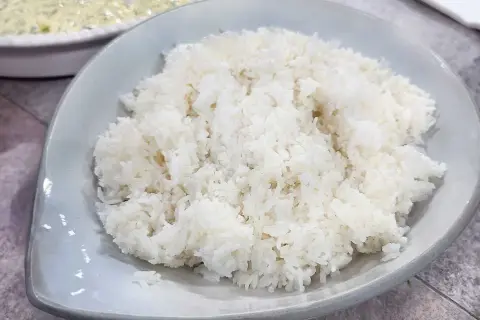 Perfekt fluffigt ris, enkelt att laga mat i riskokare. En skål med vitt ris står framför en annan skål med mat.