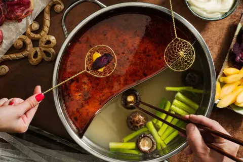 En person lägger ner grönsaker i en hot pot med två olika buljonger. Ett perfekt hot pot recept för en mysig kväll.