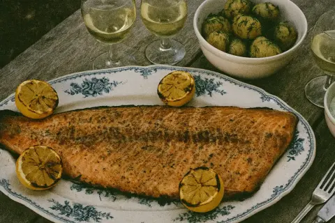 En stor grillad laxsida med citronklyftor på ett vackert fat. Serveras med dillpotatis, vit sås och vitt vin.