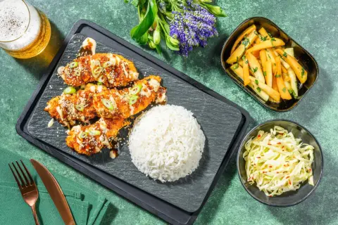 Krispig koreansk kyckling med sesamfrön och salladslök, serverad med ris, pommes frites och kålsallad.