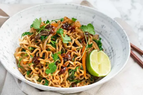 En skål med god wok med nudlar, grönsaker och en limeklyfta.