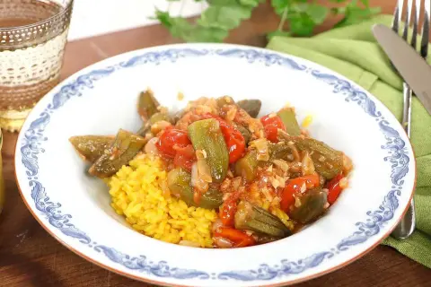 En tallrik med okra och tomater i en kryddig sås, serverad med gul ris. Ett läckert bamya recept för en smakrik måltid.