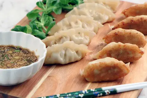 En rad gyllene, stekta dumplings och ångade dumplings serveras med en dippsås och grönsaker. Ett perfekt dumplings recept för en god måltid.