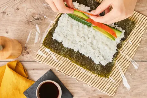 Händer lägger lax och gurka på ris för sushi maki.