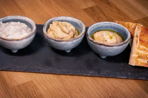Tre skålar med dippar, som tzatziki och hummus, serveras med bröd. Perfekt för ett meze recept.