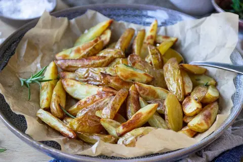 Klyftpotatis i airfryer, gyllene och krispiga, serverade med färsk rosmarin. Perfekt som tillbehör!