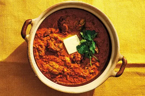 En mustig kycklingrätt i en keramikskål, toppad med en smörbit och koriander. Detta är vad "masala" betyder – en kryddblandning som ger djup och smak.