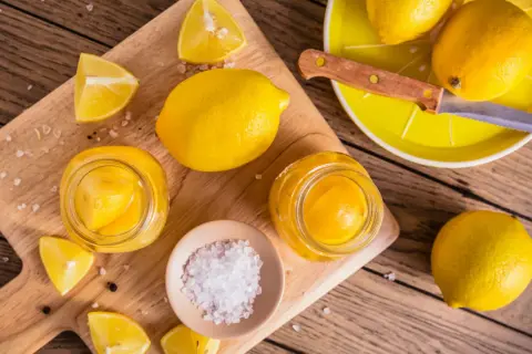 Gör ett läckert recept med inlagda citroner! Färska citroner, salt och pepparkorn förbereds på en träskärbräda.