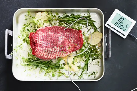 Råstek med örter och vitlök i ugnsform, redo för grillen. En digital termometer ger exakta grill tips för perfekt resultat.