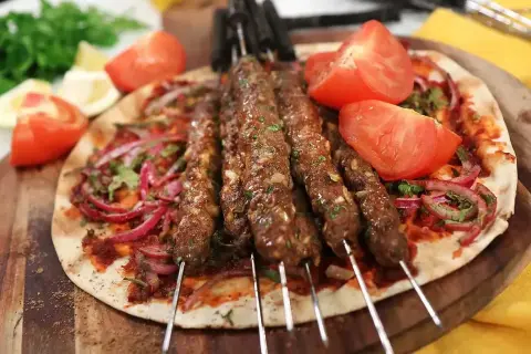 Grillad adana kebab på spett, serverad med tunnbröd, rödlök, tomat och persilja. Ett perfekt adana kebab recept för sommaren.