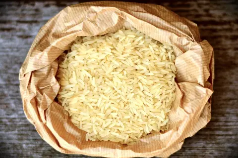 En påse med basmati eller jasminris ligger på en träyta. Riset är ljust och kornen är långa och smala.