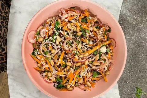 En färgstark ris sallad med jordnötter, morötter, rödlök och örter i en rosa skål.