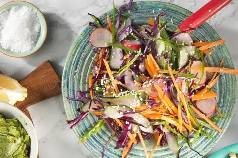 En färgglad sallad med strimlad rödkål, morot, rädisor och gurka, toppad med sesamfrön. Ett perfekt salladskål recept för en krispig och fräsch måltid.