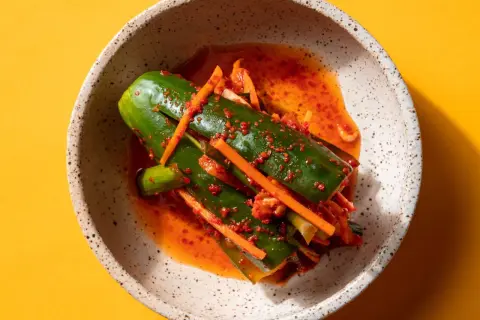 En skål med kimchi gurka, kryddad med chili och morot, på en gul bakgrund.