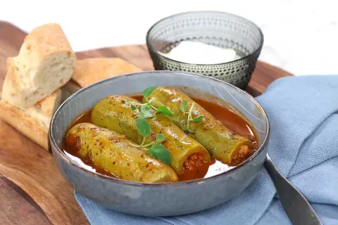 Kousa mahshi, fyllda squash i en mustig tomatsås, serveras med färskt bröd och en skål yoghurt.