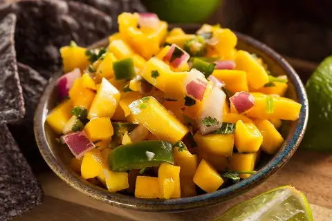 En skål med färgglad mango sallad, med tärnad mango, rödlök, grön paprika och koriander. Serveras med tortillachips och lime.