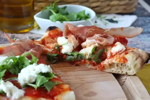 En skiva pinsa med prosciutto, mozzarella och ruccola. En härlig pinsa topping som ser utsökt ut.