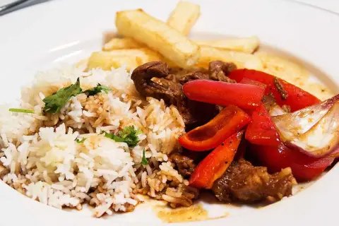 En tallrik med lomo saltado: ris, pommes frites, strimlat nötkött, rödlök och röd paprika.