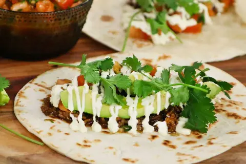 En närbild på en taco med köttfärs, avokado, koriander och en vit sås. Perfekt för ett tacokrydda recept!