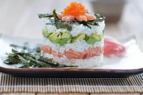 En vacker sushi tårta med lax, avokado och ris, toppad med rom och nori. En festlig rätt för alla sushiälskare.
