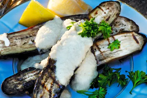 Grillad aubergine med en krämig sås och färsk persilja, serverad med citronklyftor. En härlig sommarrätt.