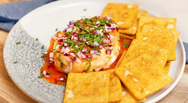 Ost med hackad rödlök och gräslök, ringlad med söt chilisås. Serveras med kex.