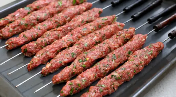 Råa kebabspett med lök och persilja ligger redo på en plåt för att tillagas i ugn.